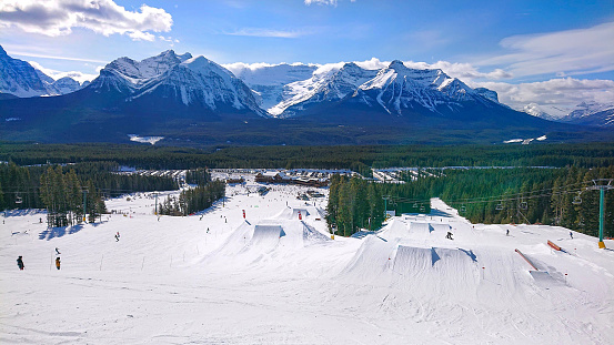 Spectacular view of an awesome snowboarding park in a ski resort in Banff, Canada. Tourists on active winter vacation have fun skiing and snowboarding around the groomed slopes and fun snowboard park.