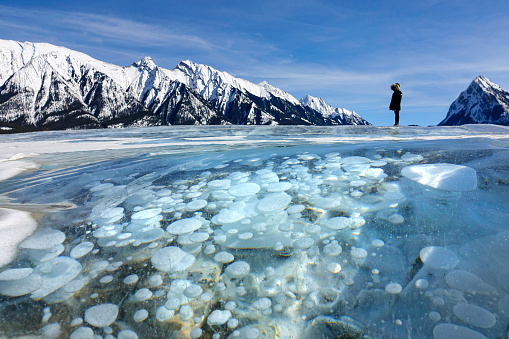 CLOSE UP: Young woman on travelling across Canada marvels at the icy lake under the Rocky Mountains. Unrecognizable female tourist observes the frozen lake Abraham filled with big methane bubbles.
