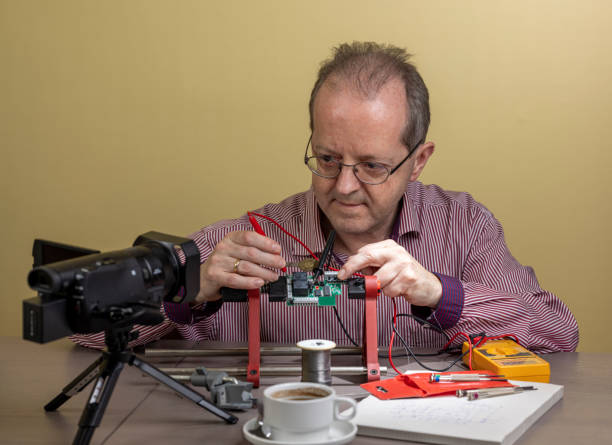 istock Middle aged man working from home, vlogging electronic repair instructions as side hustle for his social media followers on youtube 1300899774
