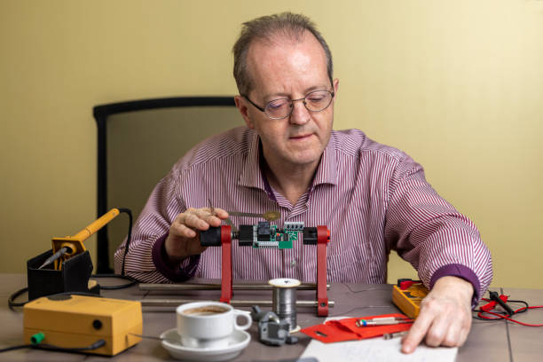 istock Reading from his notes, a repairman of middle age is working from home, soldering electronic circuit board PCB as as side hustle while staying at home due to Coronavirus 1300899799