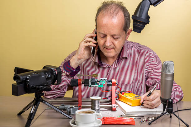 istock Talking on his mobile phone, a middle aged man is working from home, vlogging electronic repair instructions as side hustle for his social media followers on youtube 1300900799