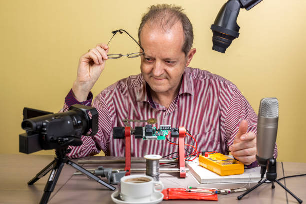 Middle aged man working from home, vlogging electronic repair instructions as side hustle for his social media followers on youtube