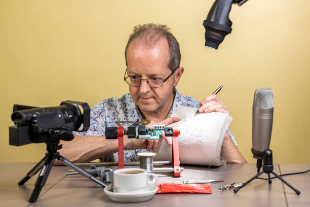 istock Presenting his notes and schematic electronic diagram to the viewers ,a middle aged man is working from home, vlogging electronic repair instructions as side hustle for his social media followers 1300900846