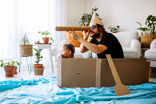 Playful childhood. Little girl and young father having fun with cardboard box. Daughter and father pretending to be on ship
