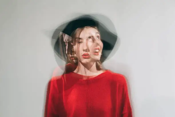 Defocused female portrait. Personality disorder. Art fashion. Tranquility thoughts. Silhouette woman in red sweater black hat sad serious happy isolated on neutral double exposure blur.
