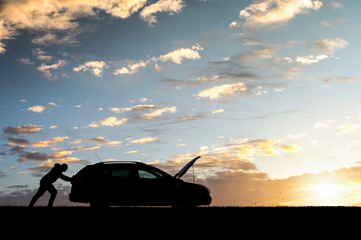 A silhouette of a man beside his vehicle having mechanical problem. Man have car engine problem on the country road at sunset