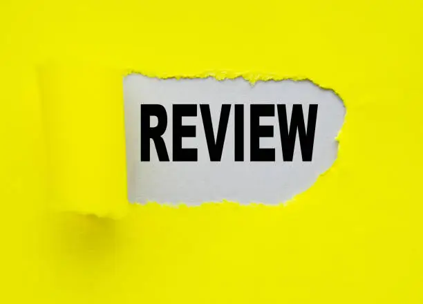 Photo of Yellow torn paper with a hole and the word REVIEW on a gray background, the concept OF ANALYSIS AND VERIFICATION