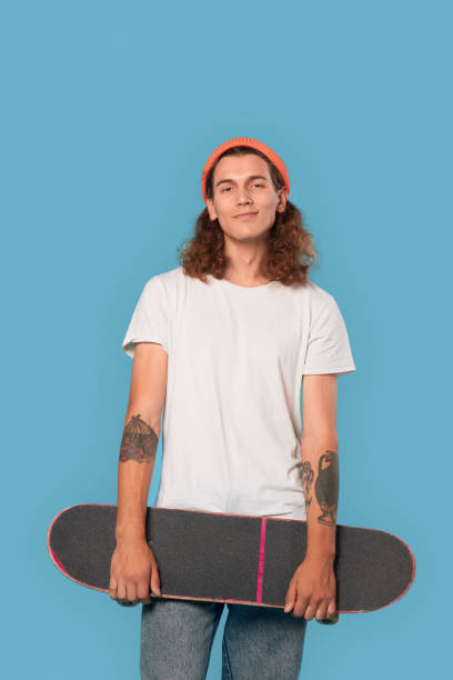 istock Freestyle. Curly-haired guy wearing hat standing isolated on blue with skateboard smiling confident 1300906808