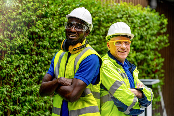 istock team factory worker technician engineer men standing confidence with green working suite dress and safety helmet. Background of green trees wall. 1300910216