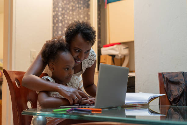 afro mutter hilft ihrer 5-8-jährigen afro-tochter ihre hausaufgaben auf ihrem laptop während covid 19 quarantäne zu tun - 9 year old stock-fotos und bilder