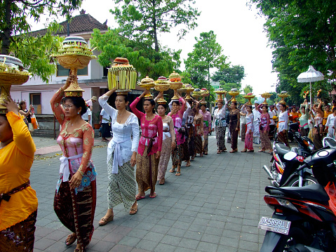 Photo of a colorful group of Balinese women, dressed in traditional temple clothing, balancing offerings on their heads and walking in a procession after the ceremony in the Market temple in Ubud, Bali.