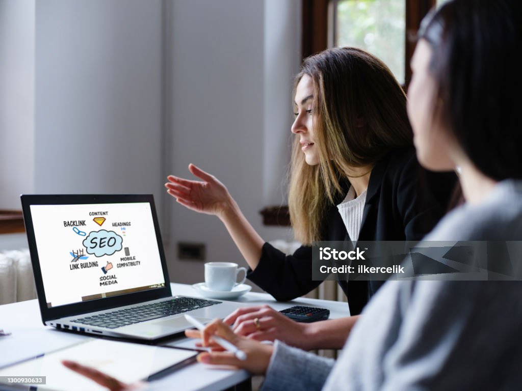 Search Engine Optimization (SEO) Concept On Computer Screen With Two Businesswomen  In The Office Search Engine Stock Photo