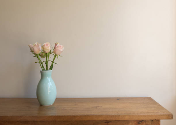 istock Pale pink roses in green vase on oak table with copy space 1300936444