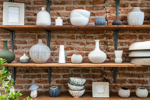 Set of clay pot and ceramic kitchenware which is kept on the wooden shelf in red brick wall storage room. Interior object photo.