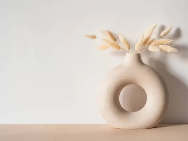 Photo of Round stylish ceramic vase with dried flower lagurus