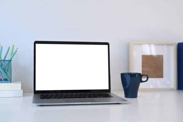 istock Mock up laptop computer with blank screen, coffee cup and books on white office desk. 1300943117