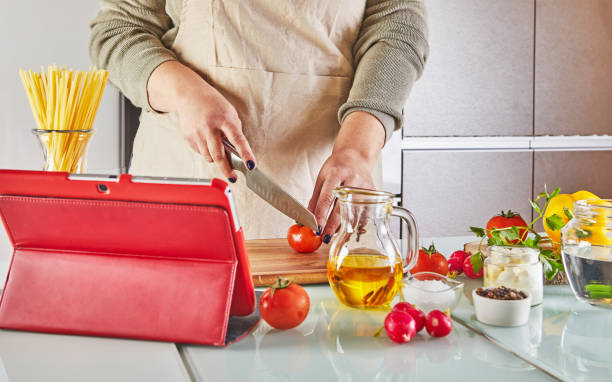 Woman cooking according the tutorial of online virtual master class, And looking on the digital recipe, using touchscreen tablet while cooking healthy meal on the kitchen at home