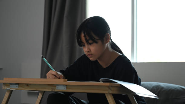 istock Young school girl doing homework assignment on bed at home. 1300945565