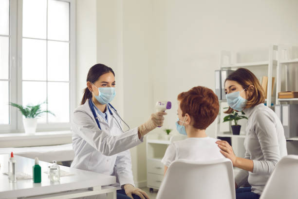 friendly doctor measuring little child's temperature with non-contact infrared thermometer - pre adolescent child child group of people little boys imagens e fotografias de stock