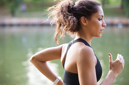 Side view of young woman in sports bra jogging by the river in public park