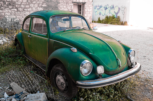 Trikala, Greece - February 6, 2021: An old abandoned green-coloured classic Volkswagen Beetle with flat tire left in a yard.