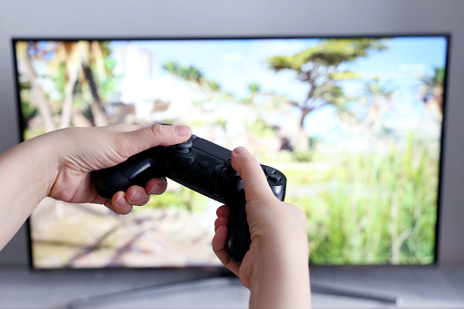 Gamepad in female hands closeup on TV screen background, gaming addiction concept