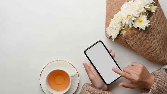 Top view of female touching on smartphone screen on coffee table with tea cup and flower brunch