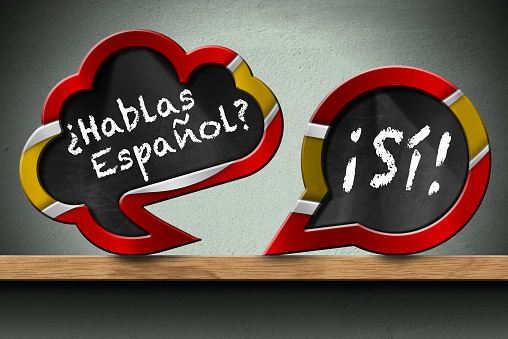 3D illustration of two speech bubbles with Spanish flag and question Hablas Espanol? and Si! (Do you speak Spanish? and Yes!). On a wooden shelf with a wall on background.
