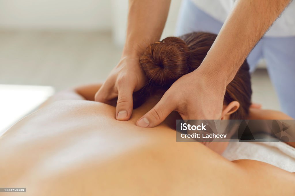 Young woman enjoying relaxing remedial body massage done by professional masseur Close-up of woman lying on massage table face down enjoying spa procedures. Young female patient receiving professional remedial body massage in massage room of modern wellness center Massaging Stock Photo