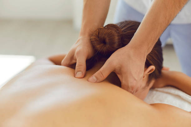Young woman enjoying relaxing remedial body massage done by professional masseur Close-up of woman lying on massage table face down enjoying spa procedures. Young female patient receiving professional remedial body massage in massage room of modern wellness center shiatsu stock pictures, royalty-free photos & images
