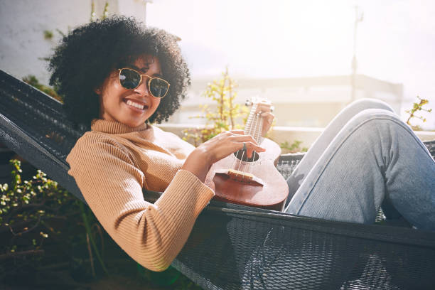 Portrait of a young woman playing ukulele while relaxing on a hammock