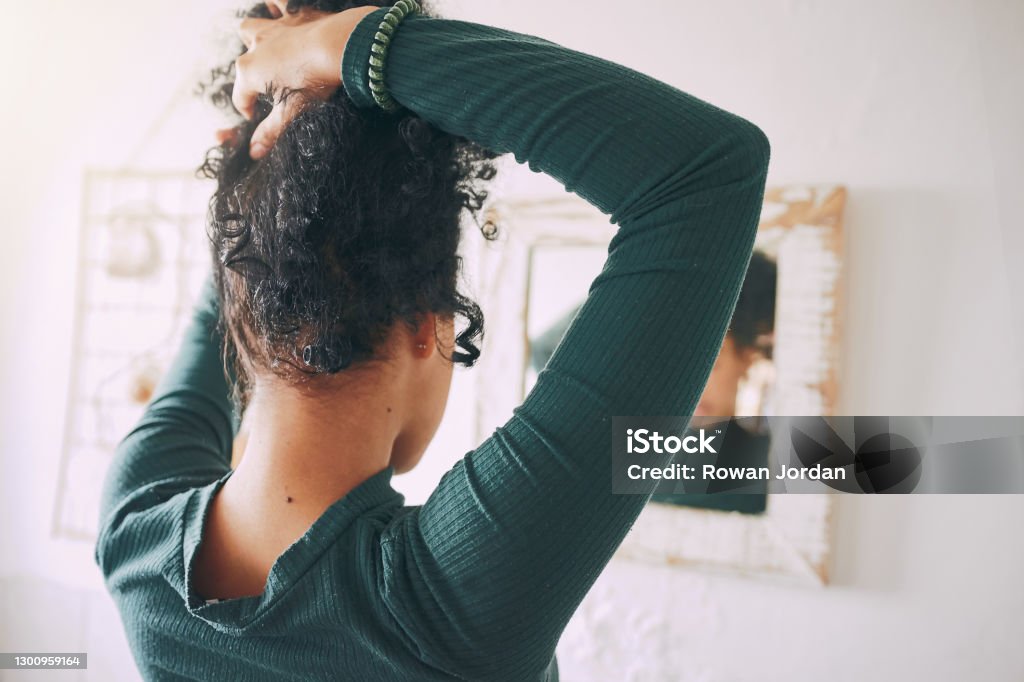 What hairstyle should I rock today? Rearview shot of a young woman tying her hair in the bathroom at home Women Stock Photo