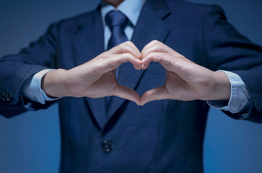 Smart Businessman wear blue suit shirt and tie making heart shape by his hand on blue background. Handsome man show heart symbol, love icon for Business lover, I love my job, take care service concept.