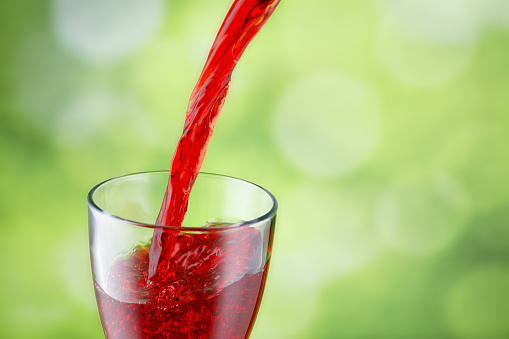pomegranate juice pouring into glass on green nature blurred background