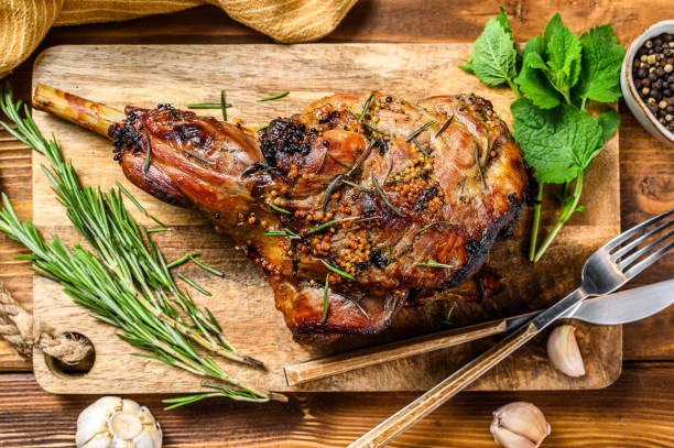 Roasted goat leg with herbs. Farm meat. Wooden background. Top view. Copy space Roasted goat leg with herbs. Farm meat. Wooden background. Top view. Copy space. celebrity roast stock pictures, royalty-free photos & images