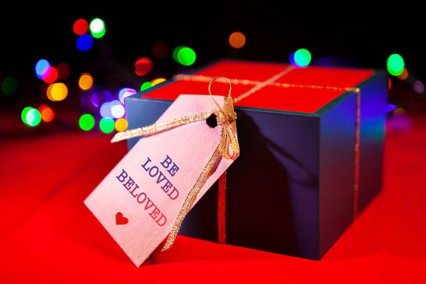 istock Gift box label with text - be loved beloved, red background with colorful lights from the back. 1300960609