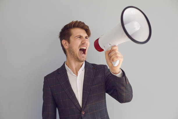 istock Stylish executive man screaming with loudspeaker on gray background 1300960692