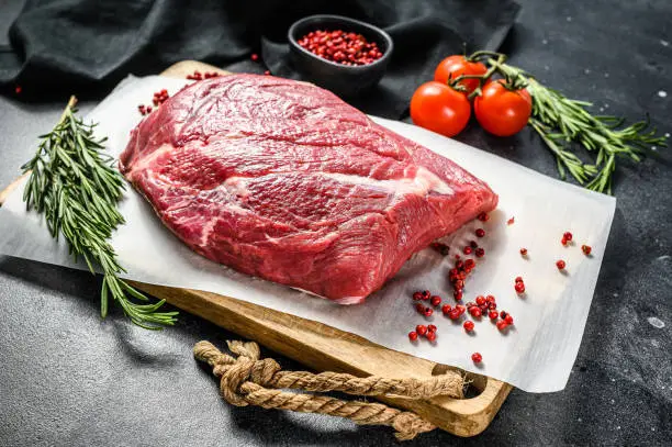 Raw brisket beef cut on a wooden cutting board. Black Angus beef. Black background. Top view.