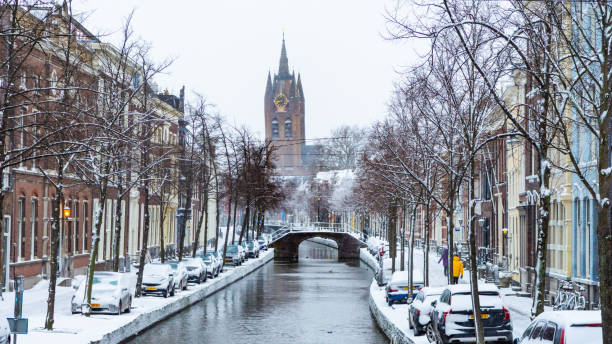 Delft, Netherlands - Snow in the city center with a canal in downtown, church and traditional dutch houses Old city center of Delft (Zuid-Holland, Netherlands). View of the canal (Oude Delft) with tipical dutch houses. Behind the old brige is the ''Oude Kerk''. delft winter netherlands snow stock pictures, royalty-free photos & images