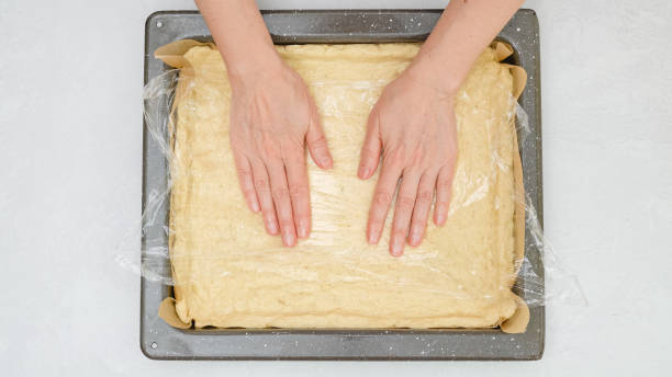 istock Woman's hands placing pizza dough onto baking pan, close up view from above with copy space 1300961866