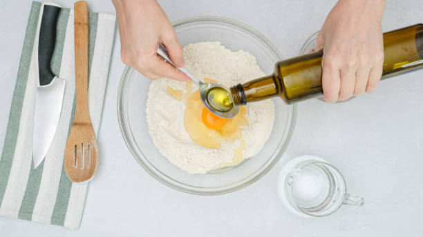 istock Bowl with flour, yeast and eggs close up on kitchen table. Woman's hands add olive oil into a bowl, flat lay 1300961867