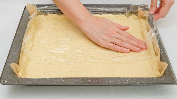 istock Using a plastic wrap chef  unfurl pizza dough onto a baking pan. Close up step by step homemade pizza recipe 1300961935