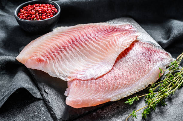 istock Fresh tilapia fillet on a chopping Board with thyme. Black background. Top view 1300964641