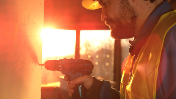 close up lens flare: kaukaski budowniczy odkręca śrubę utkniętą w panelu ściennym. - machine equipment work tool drill bit zdjęcia i obrazy z banku zdjęć