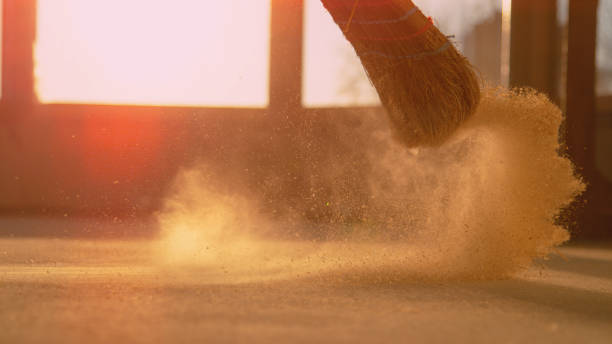 LOW ANGLE: Dust gets swept up into air as person cleans a construction site LENS FLARE, CLOSE UP, LOW ANGLE: Dust gets swept up into air as an unrecognizable person cleans the construction site floor. Contractor sweeps the ground of a construction site with a straw broom broom photos stock pictures, royalty-free photos & images