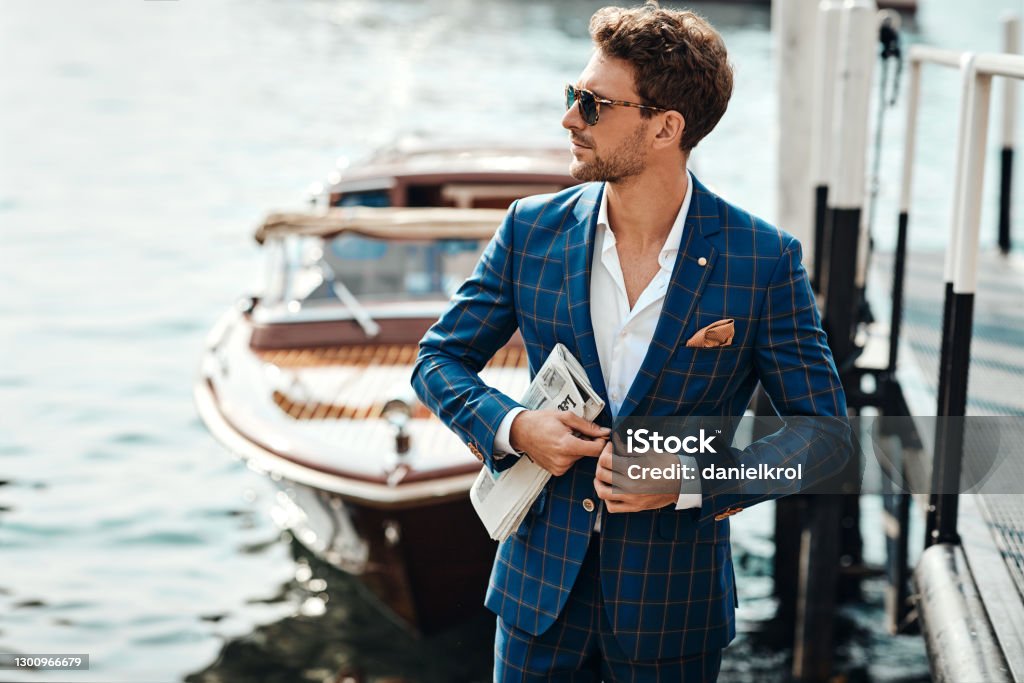 Young handsome man in classic suit over the lake background Young handsome man in classic suit over the blurred lake buttoning his jacket Men Stock Photo
