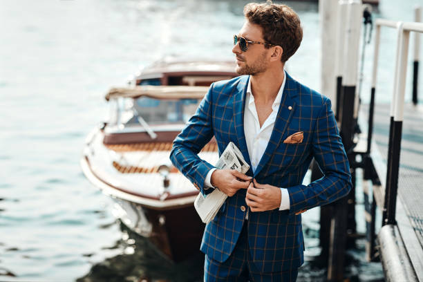 Young handsome man in classic suit over the lake background Young handsome man in classic suit over the blurred lake buttoning his jacket sailboat photos stock pictures, royalty-free photos & images