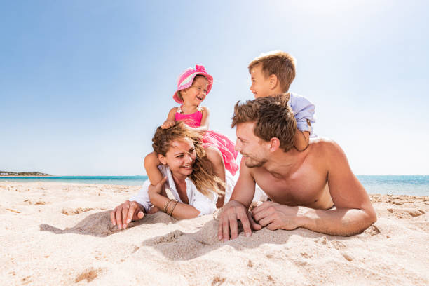 istock Young happy family talking while relaxing in sand on the beach. 1300969942