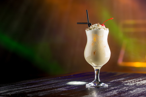 Pina Colada cocktail with whipped cream and cherry on the table in nightclub background side view