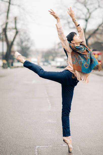 Japanese ballerina performs ballet arabesque pose among the city street.